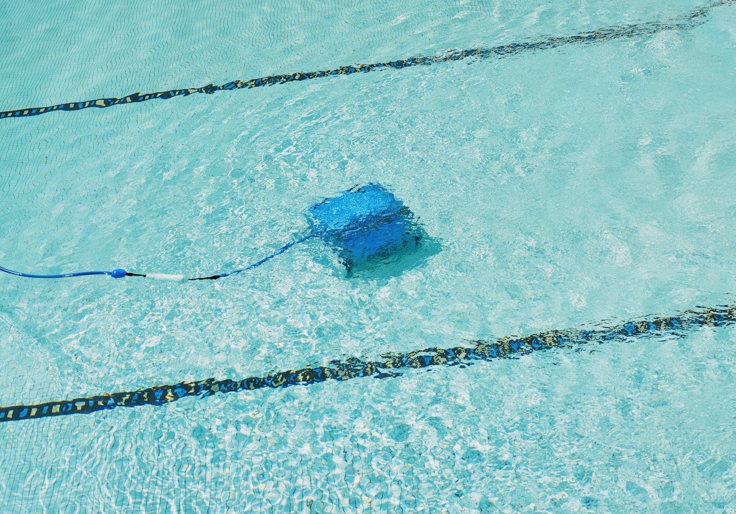 A blue robotic pool cleaner moves along the tiled pool floor.