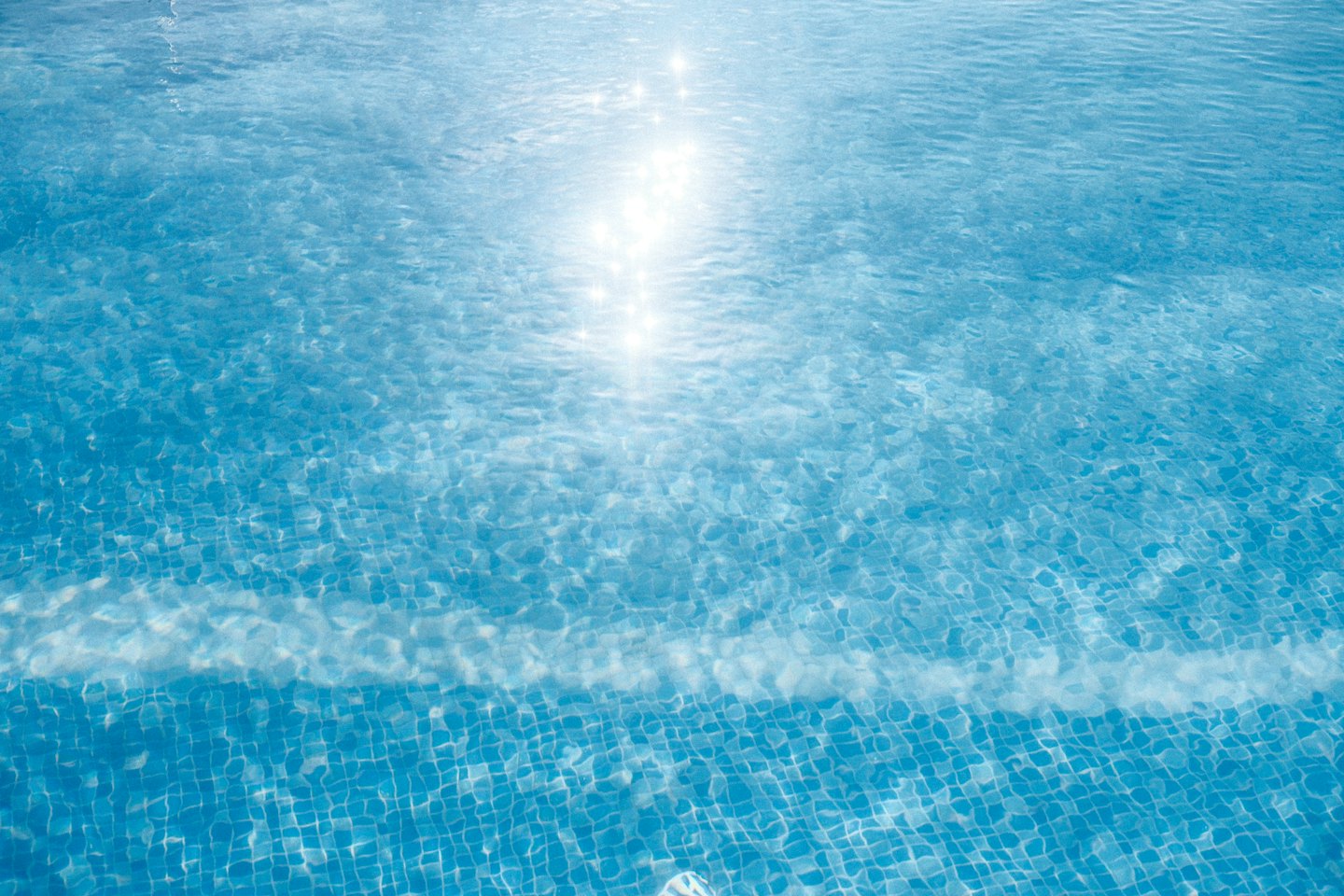 Sunlight ripples across the surface of a blue tiled pool.