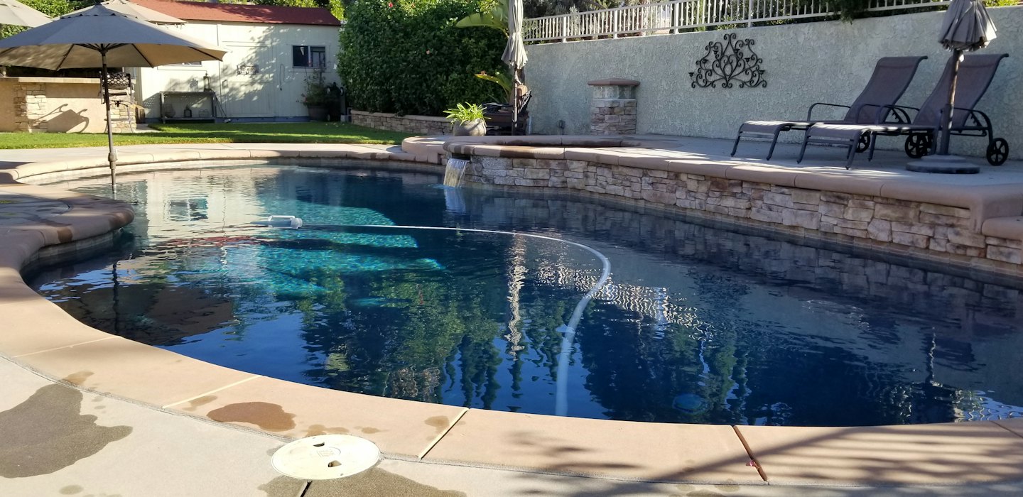 Robotic pool cleaner in a backyard pool with a waterfall.