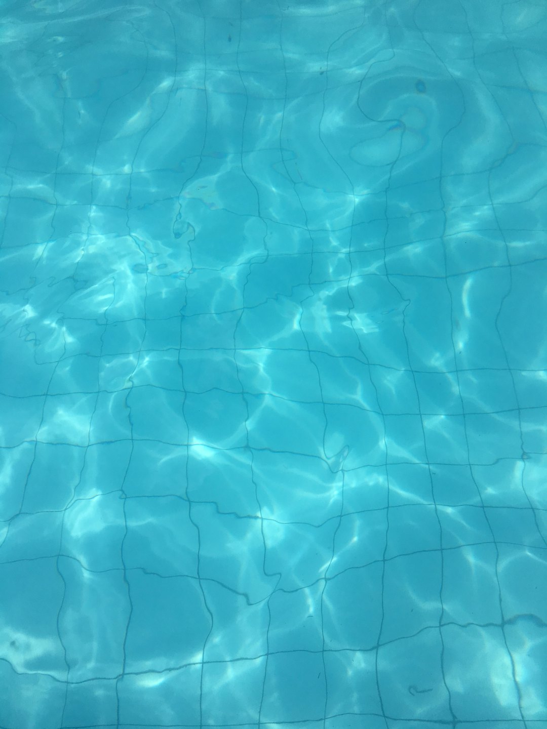 Sunlight reflects across the blue tiled bottom of a pool.